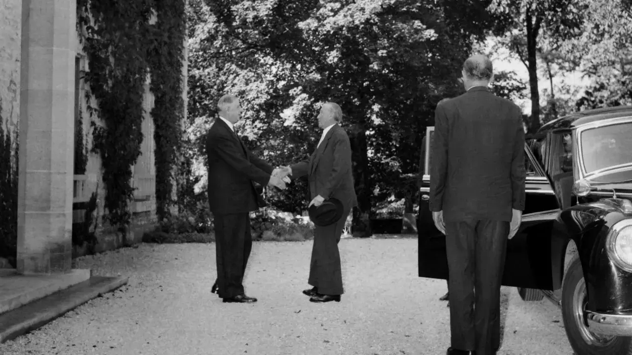 Konrad Adenauer und Charles de Gaulle schütteln sich die Hände. Ein Mann im Anzug steht daneben.