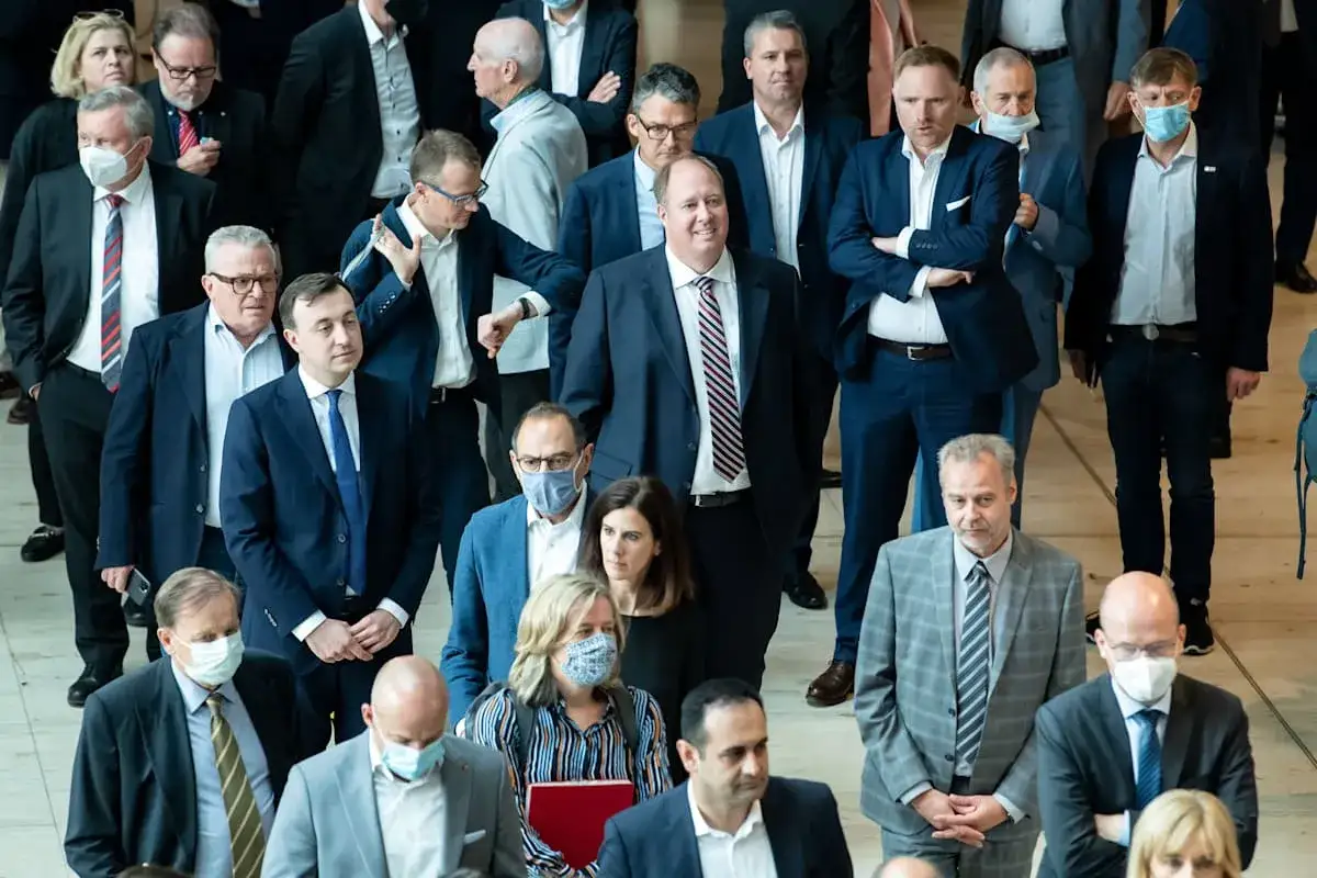 Abgeordnete im Bundestag, einige mit Masken, stehen dicht gedrängt. Ein Mann in dunklem Anzug und gestreiftem Hemd blickt nach vorne. Der Bundestag Hammelsprung ist ein wichtiger Moment der Abstimmung.