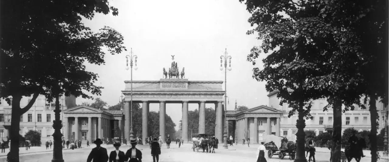 Das Brandenburger Tor, ein Wahrzeichen von historischen Orten in Berlin, mit Pferdekutschen und Menschen auf der Straße.