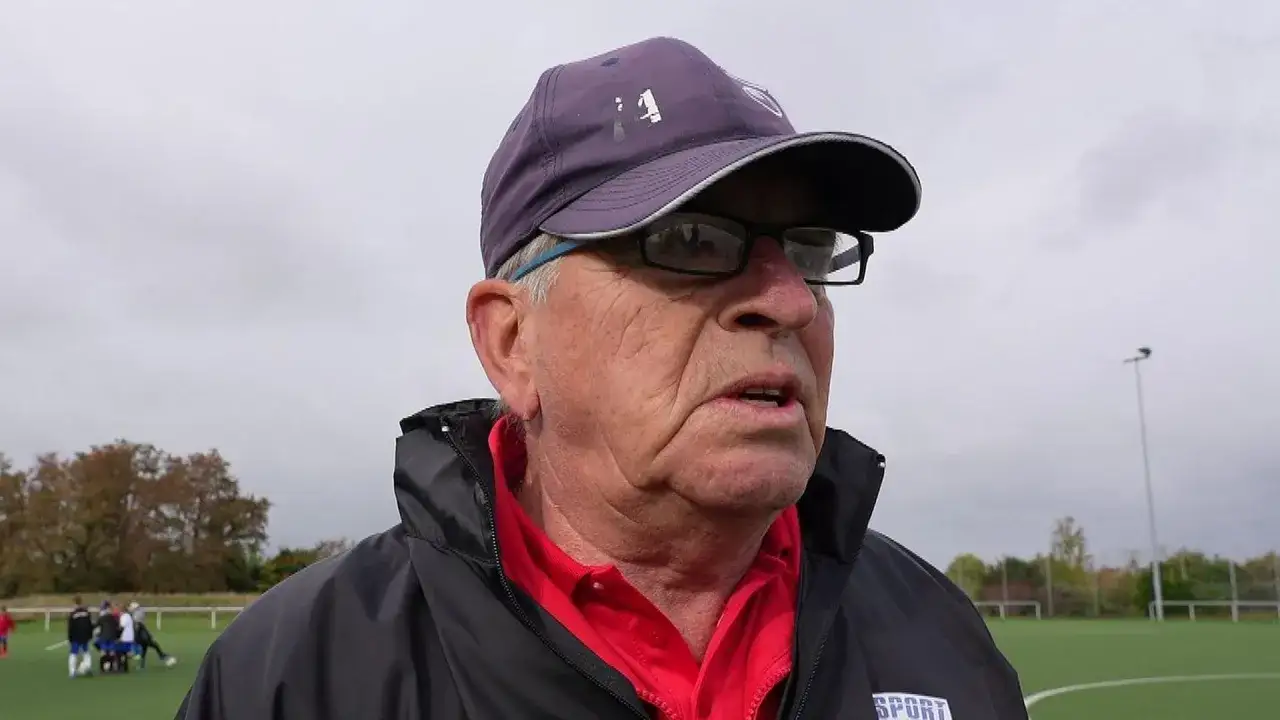 Martin Hoffmann, ein älterer Mann mit Brille und Kappe, spricht auf einem Fußballplatz.